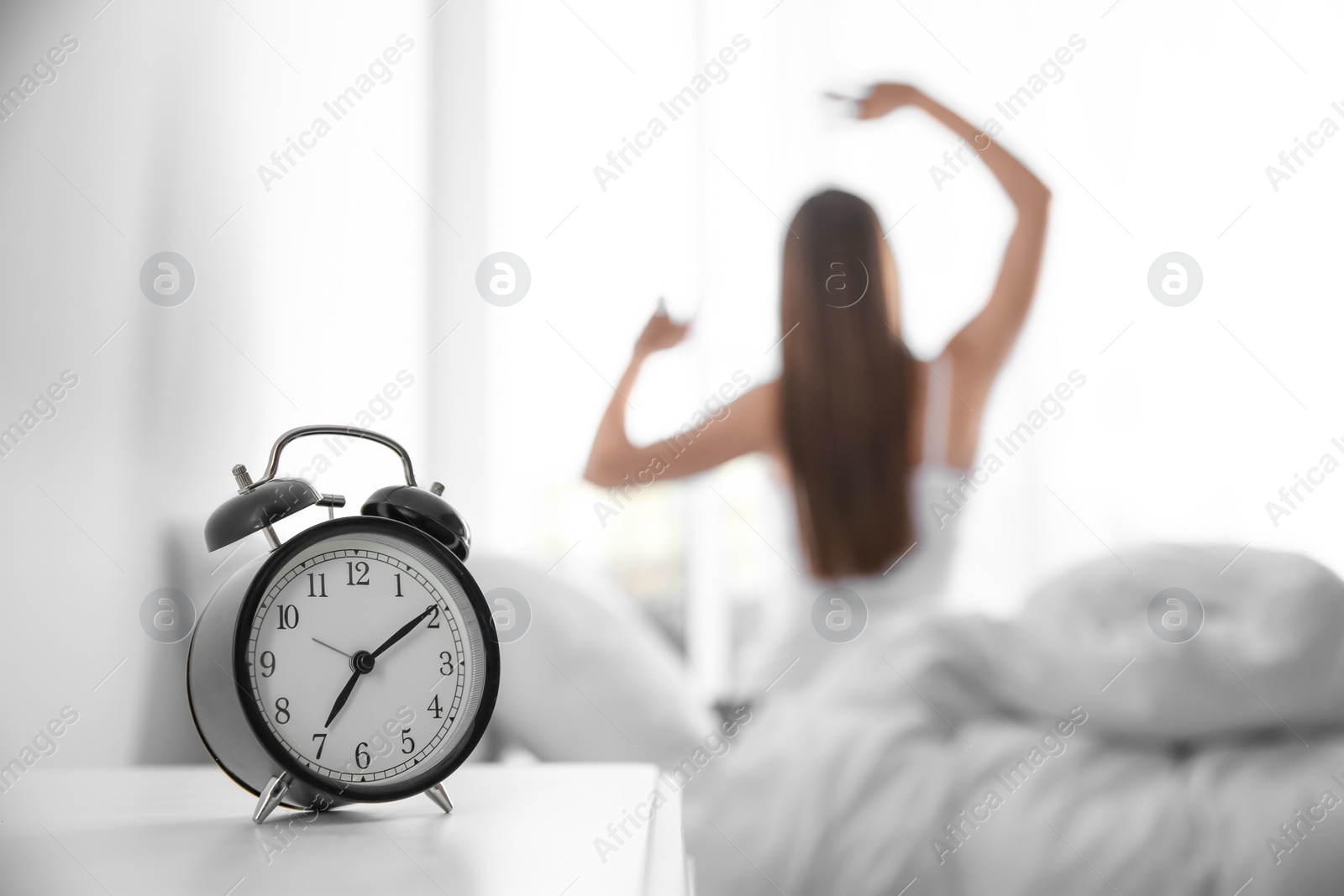Photo of Young woman stretching at home in morning, focus on alarm clock