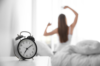 Photo of Young woman stretching at home in morning, focus on alarm clock