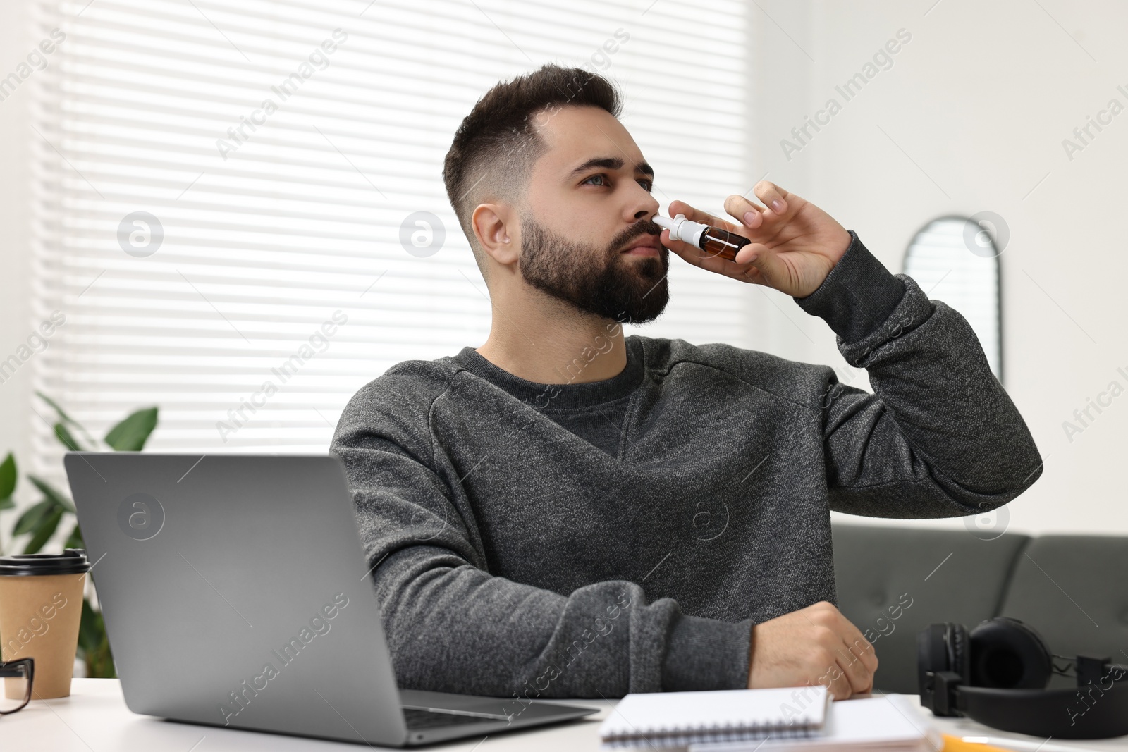 Photo of Medical drops. Young man using nasal spray at table indoors