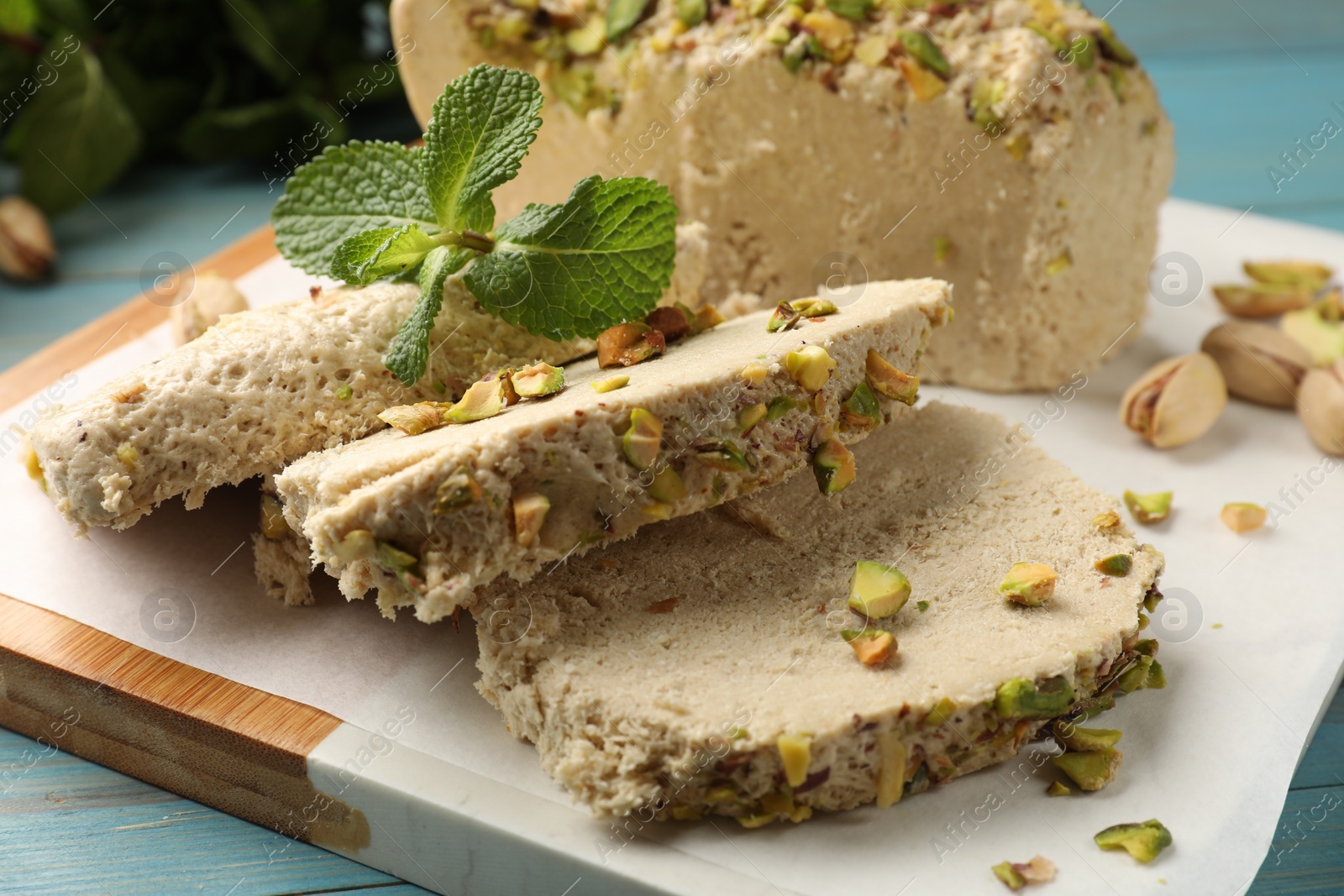 Photo of Pieces of tasty halva with pistachios and mint on table, closeup