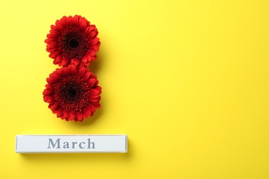 Photo of 8 March greeting card design with red gerberas and space for text on yellow background, flat lay. International Women's day