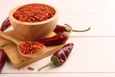 Photo of Chili pepper flakes and pods on white wooden table, closeup. Space for text