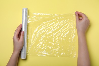 Photo of Woman with roll of stretch wrap on yellow background, top view