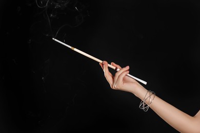 Photo of Woman holding long cigarette holder on black background, closeup