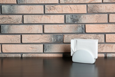 Photo of Ceramic napkin holder with paper serviettes on table near brick wall. Space for text