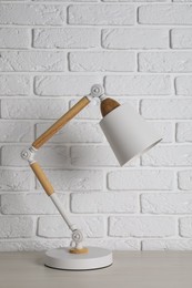 Photo of Stylish modern desk lamp on white wooden table near brick wall