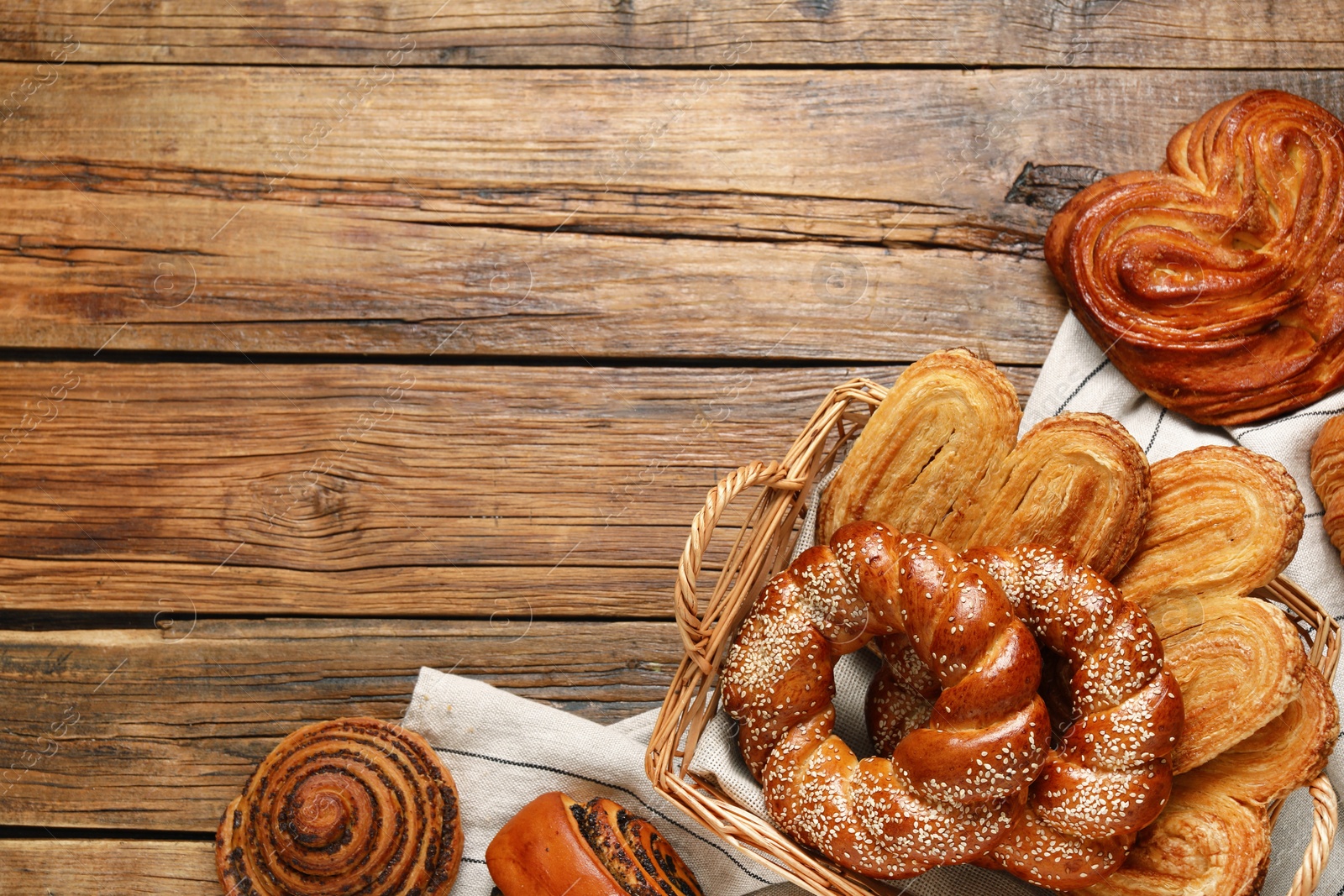 Photo of Wicker basket and different tasty freshly baked pastries on wooden table, flat lay. Space for text