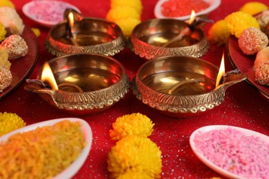 Diwali celebration. Diya lamps, tasty Indian sweets and bright rangoli on shiny red table