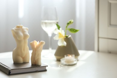 Beautiful body shaped candles and book on table indoors, space for text
