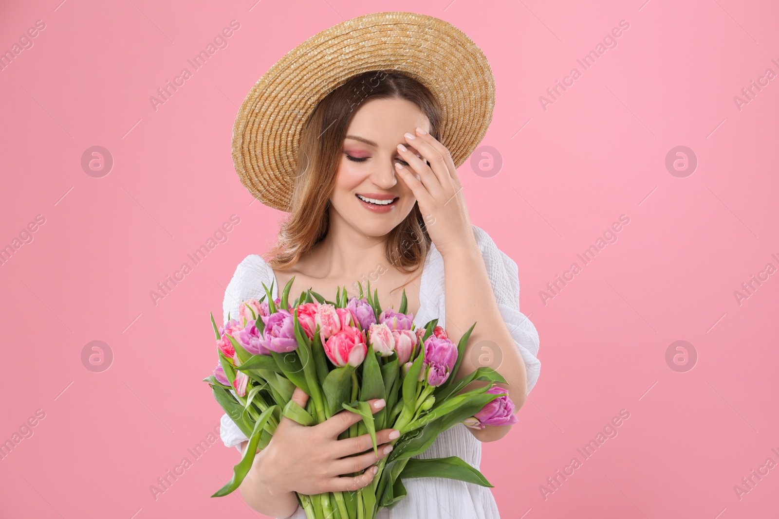 Photo of Happy young woman in straw hat holding bouquet of beautiful tulips on pink background