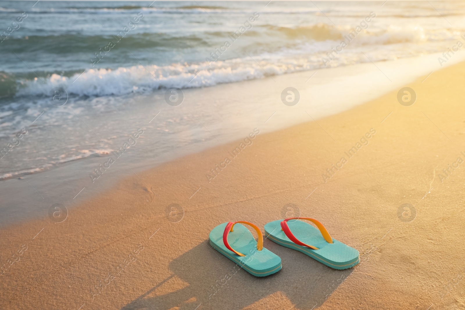 Photo of Bright turquoise beach slippers on sand near sea, space for text