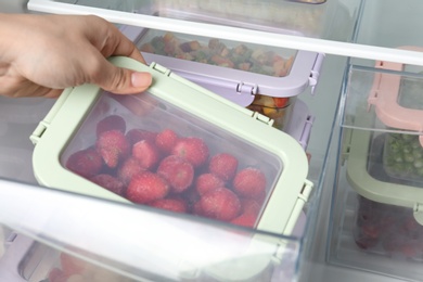 Woman taking box with frozen strawberry from refrigerator, closeup