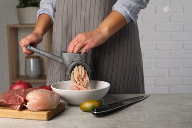 Woman making chicken mince with metal meat grinder at grey table indoors, closeup