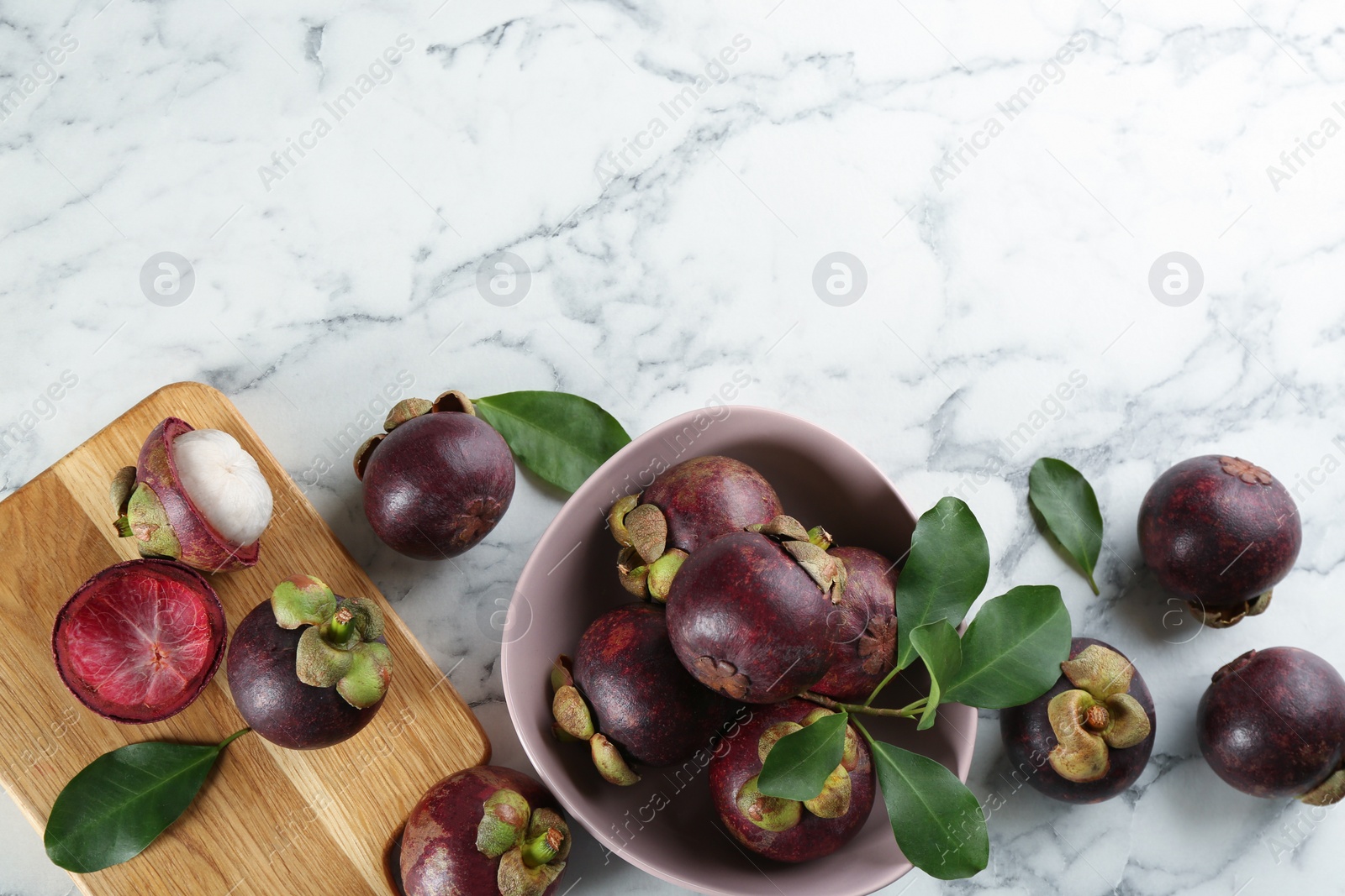 Photo of Fresh ripe mangosteen fruits on white marble table, flat lay. Space for text