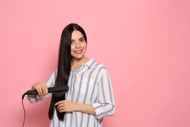 Beautiful happy woman using hair iron on pink background. Space for text