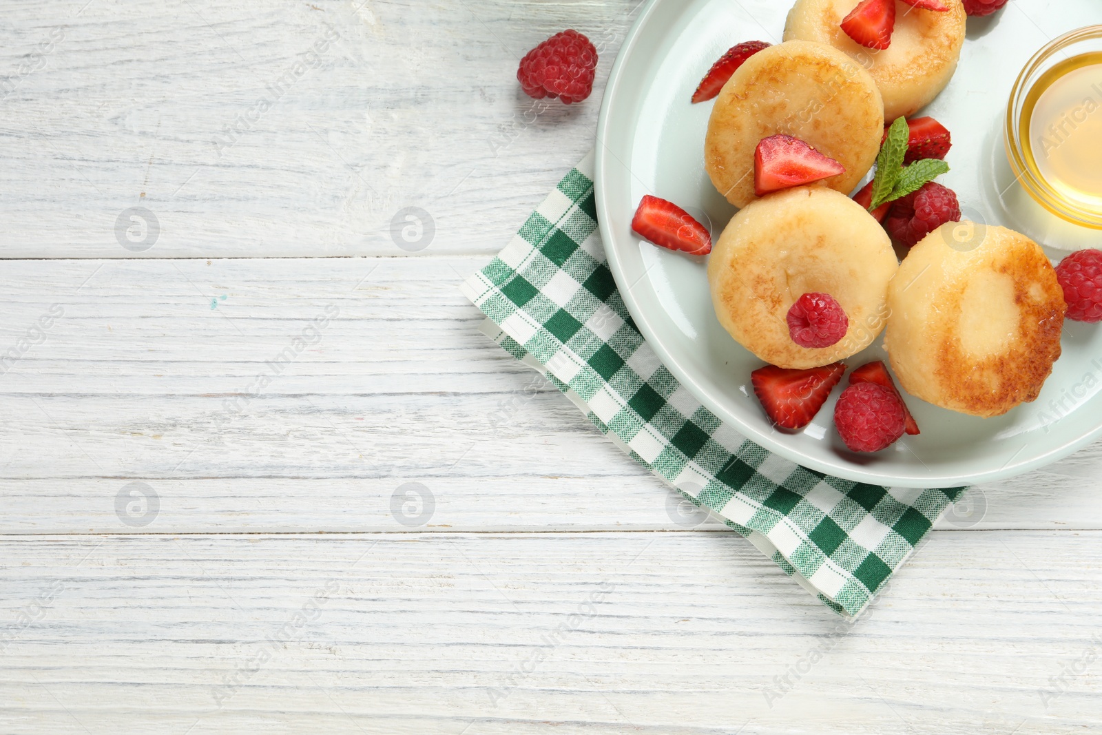 Photo of Delicious cottage cheese pancakes with fresh berries and honey on white wooden table, flat lay. Space for text
