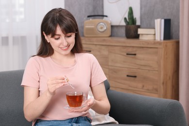 Woman dripping food supplement into cup of tea indoors, space for text