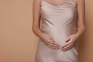Pregnant woman in dress on beige background, closeup. Space for text