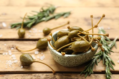 Photo of Delicious pickled capers, salt and rosemary twigs on wooden table, closeup