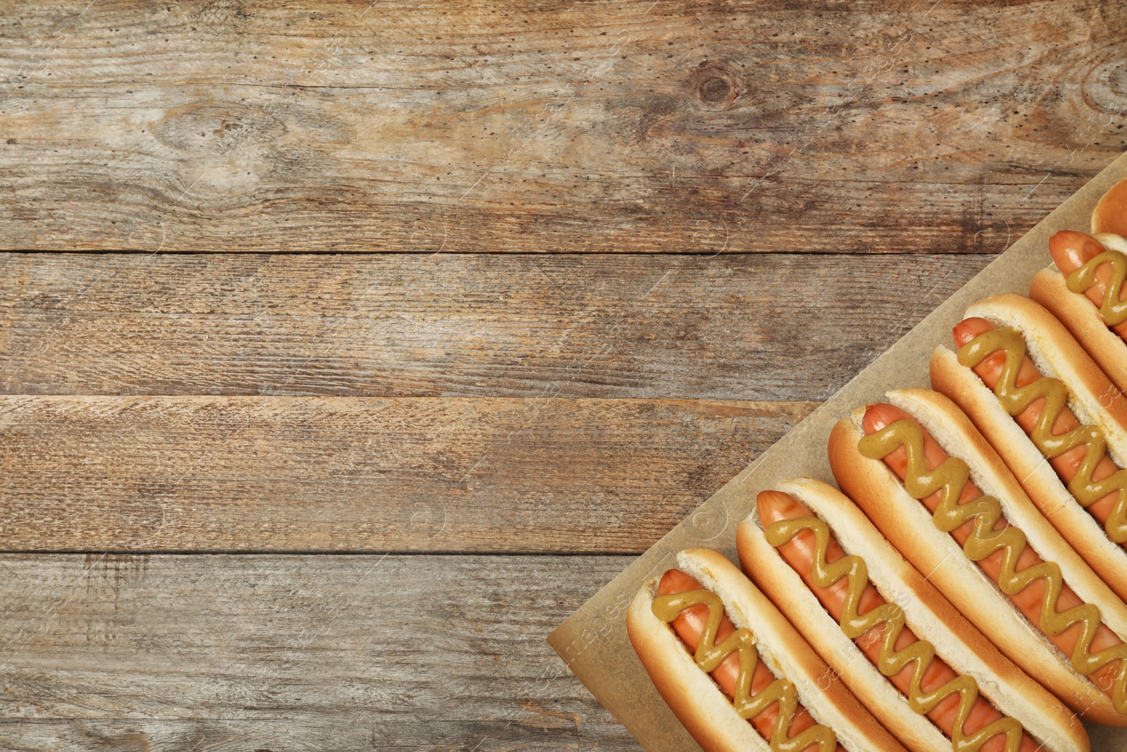 Photo of Hot dogs with mustard and space for text on wooden background, top view