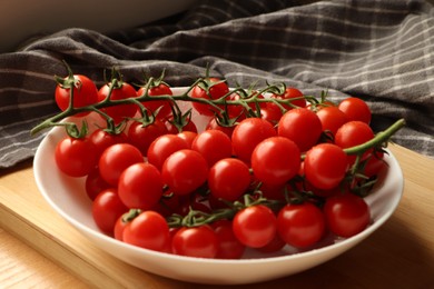 Photo of Plate of ripe whole cherry tomatoes with water drops on wooden table, closeup