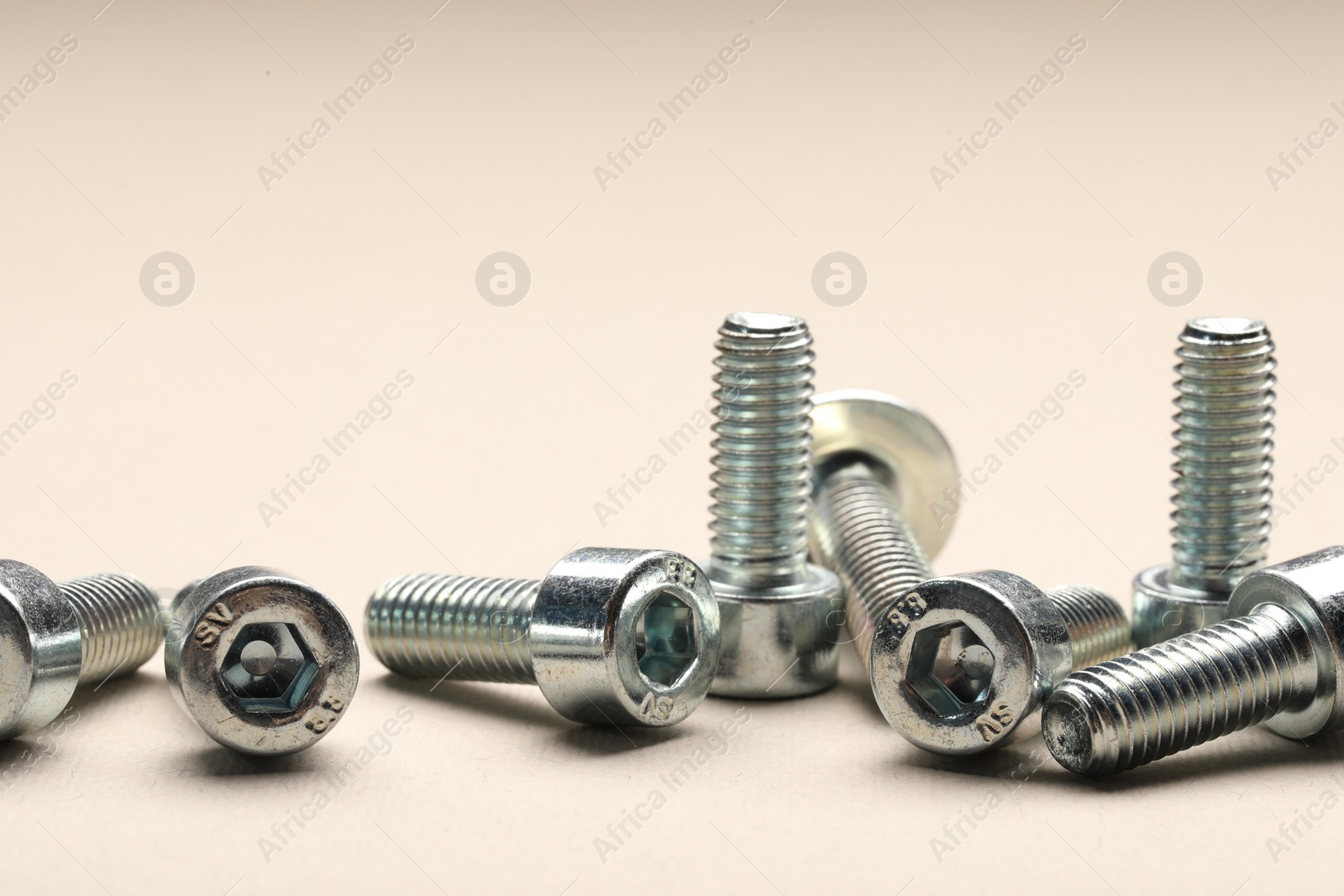 Photo of Many metal socket screws on beige background, closeup
