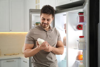 Photo of Young man with bottle of milk near open refrigerator in kitchen