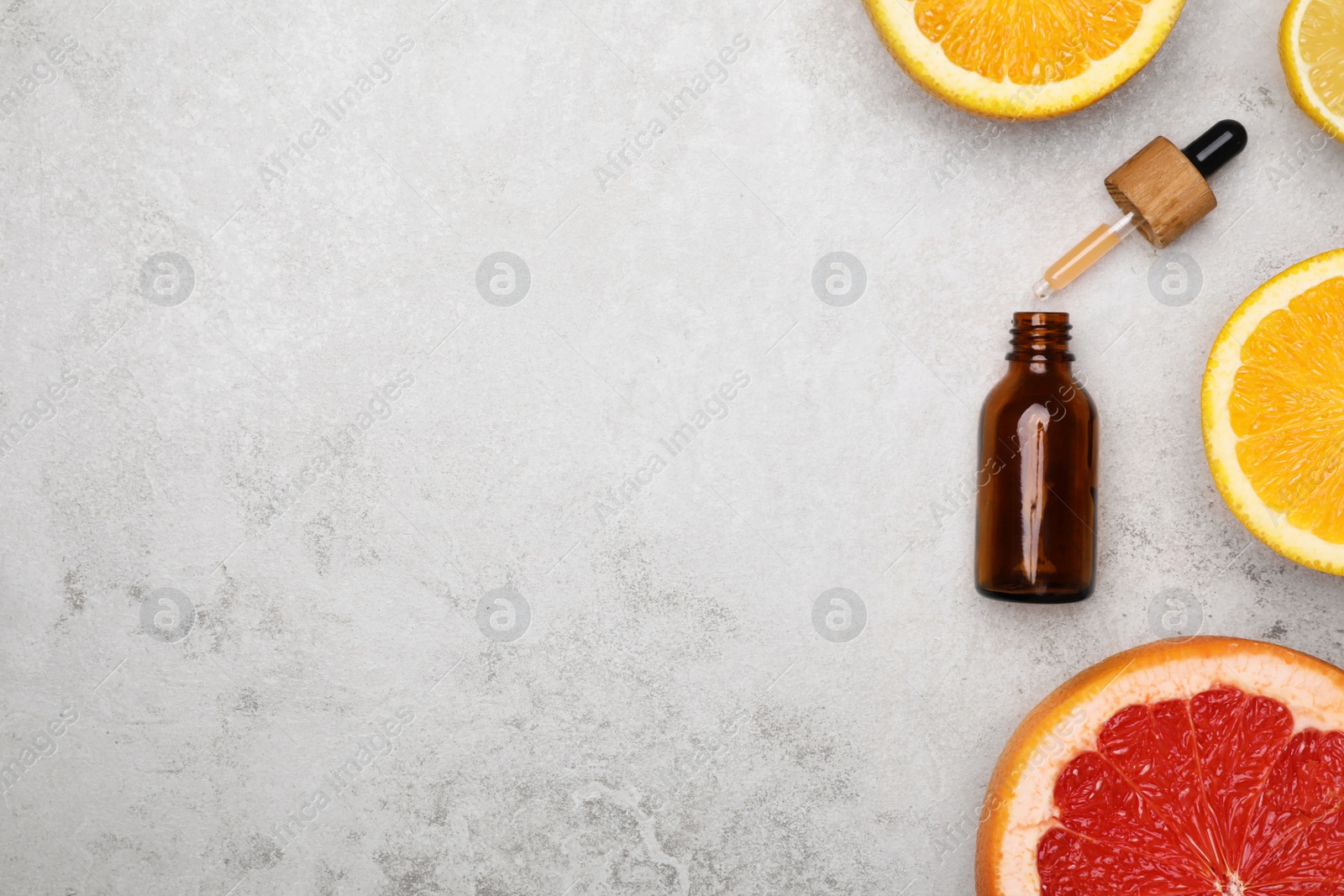 Photo of Bottle of citrus essential oil and fresh fruits on light table, flat lay. Space for text