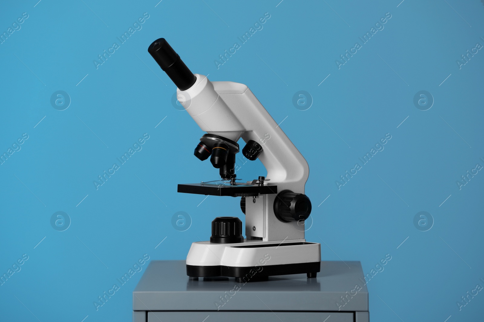 Photo of Modern microscope on table against blue background. Medical equipment