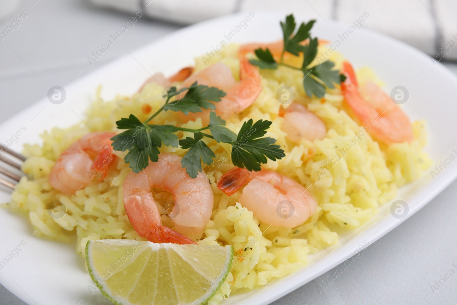 Photo of Delicious risotto with shrimps, lime and parsley on white table, closeup