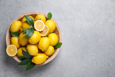Many fresh ripe lemons with green leaves on light grey table, top view. Space for text