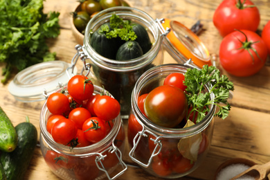 Photo of Pickling jars with fresh ripe vegetables and spices on wooden table, closeup