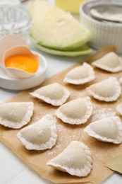 Raw dumplings (varenyky) with tasty filling and flour on parchment paper, closeup