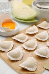 Photo of Raw dumplings (varenyky) with tasty filling and flour on parchment paper, closeup