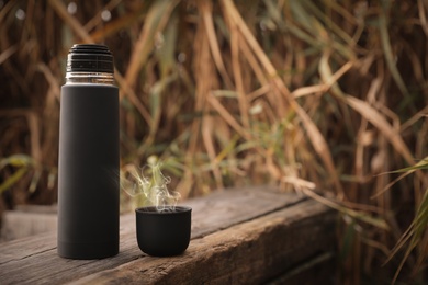 Black thermos and cap on wooden surface outdoors. Space for text