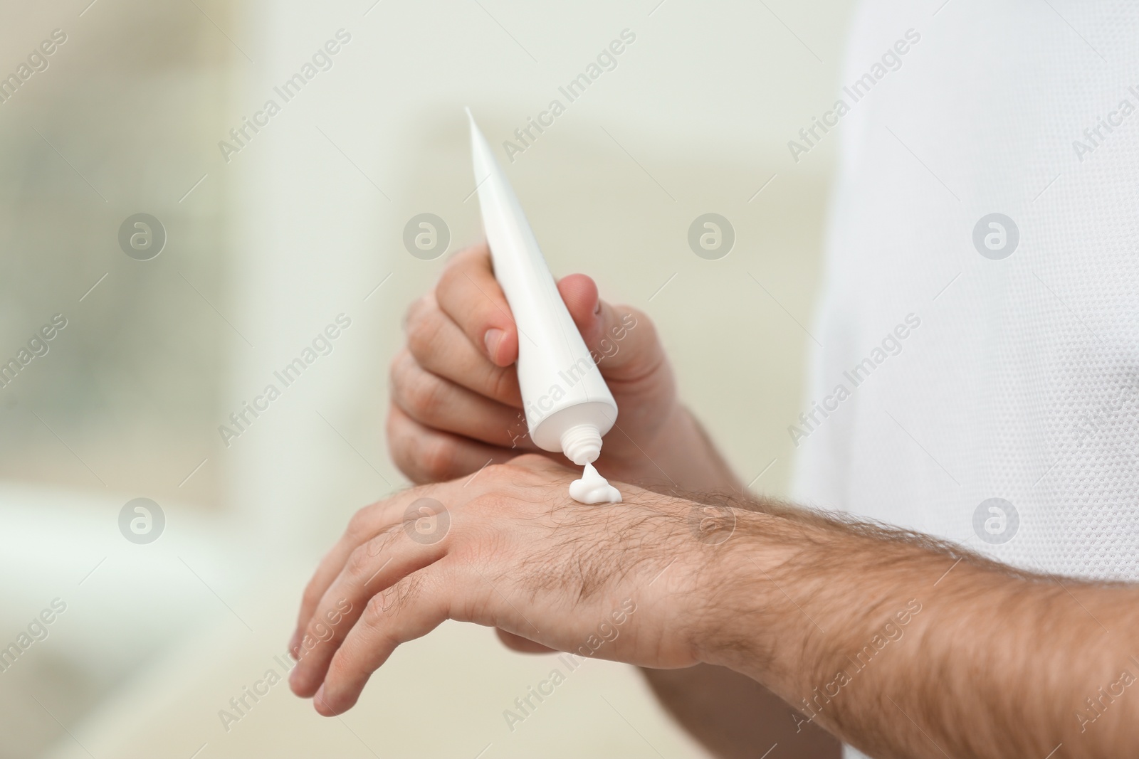 Photo of Man applying cream from tube onto hand on blurred background, closeup