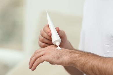 Man applying cream from tube onto hand on blurred background, closeup