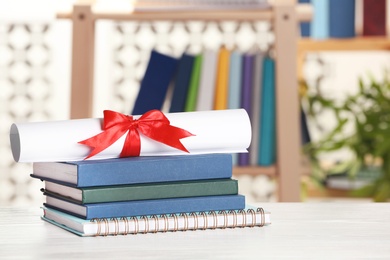 Graduate diploma with books and notebook on table against blurred background