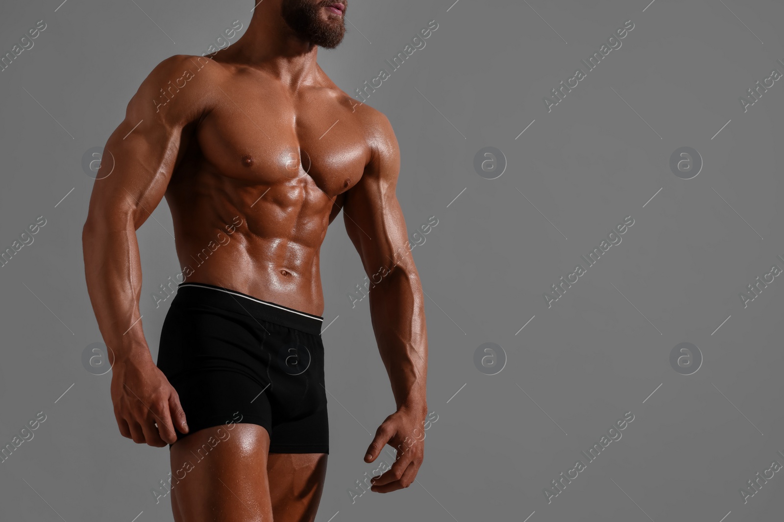 Photo of Young bodybuilder with muscular body on grey background, closeup. Space for text