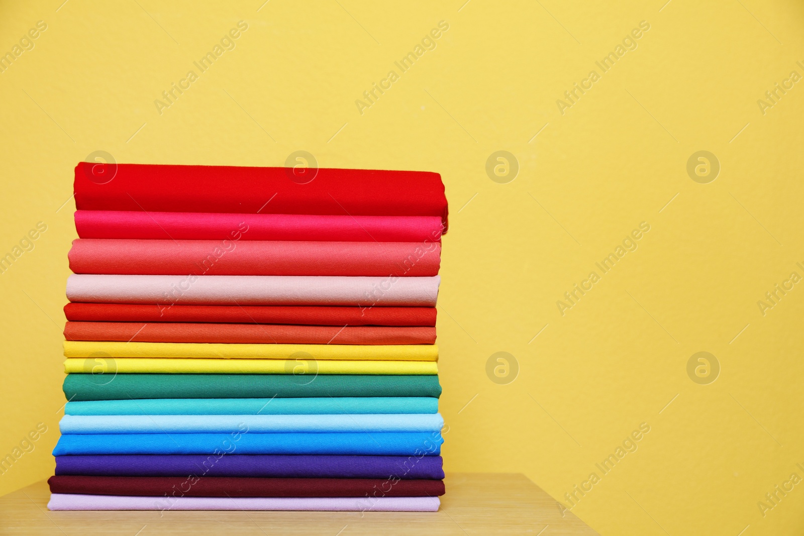 Photo of Pile of bright t-shirts on table against color background