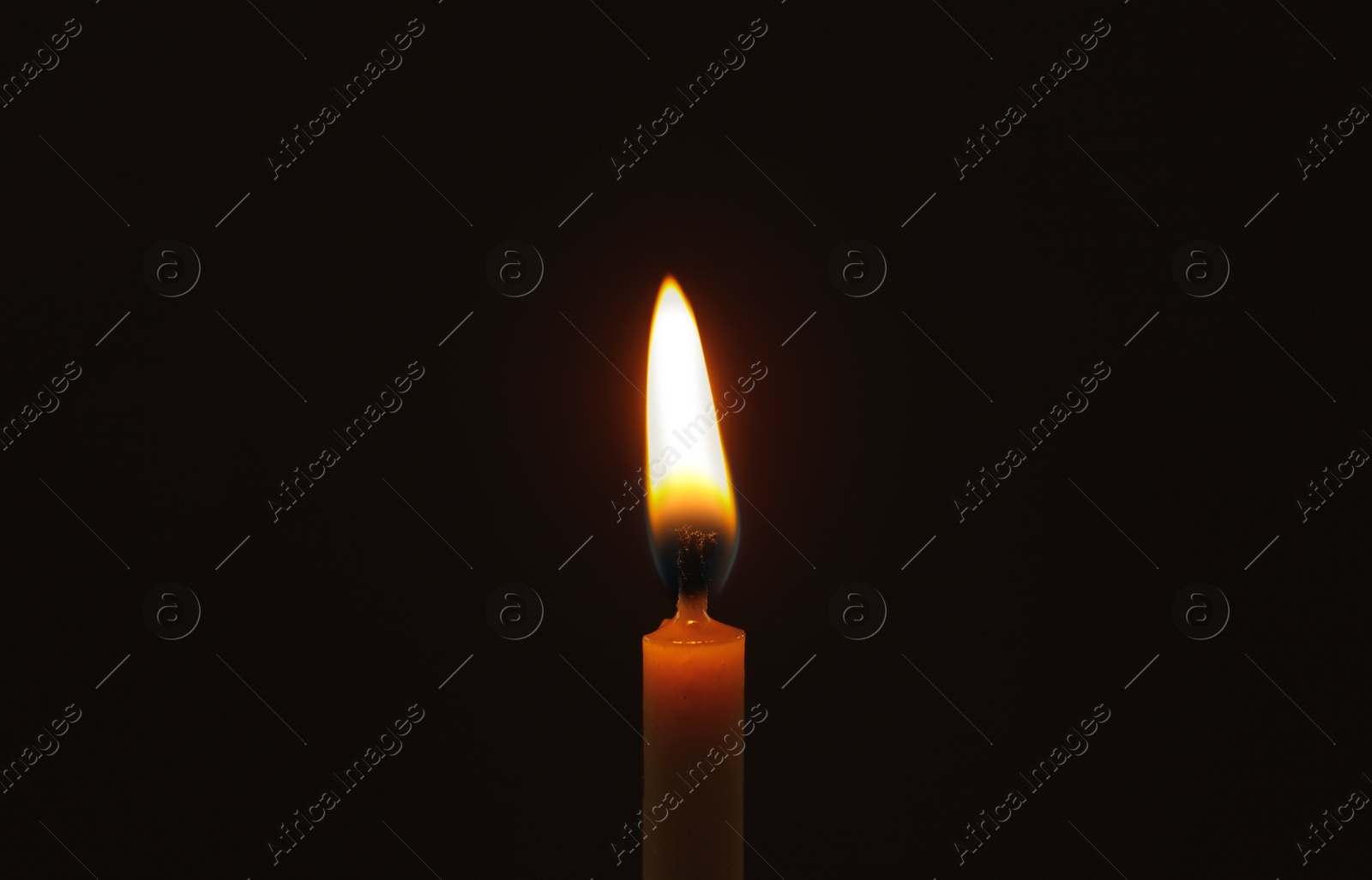 Photo of Wax candle burning on black background, closeup