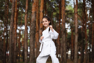 Photo of Cute little girl in kimono practicing karate in forest