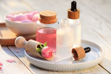 Photo of Bottles of rose essential oil and flowers on white wooden table