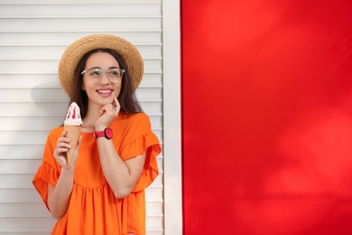 Happy young woman with delicious ice cream in waffle cone near color wall. Space for text