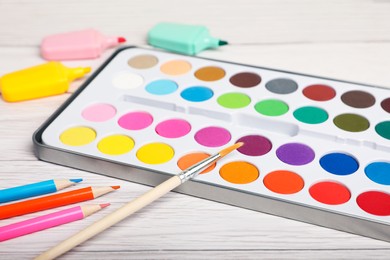 Photo of Watercolor palette with brush, colorful pencils and markers on white wooden table, closeup