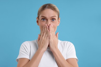Photo of Portrait of embarrassed woman covering mouth with hands on light blue background