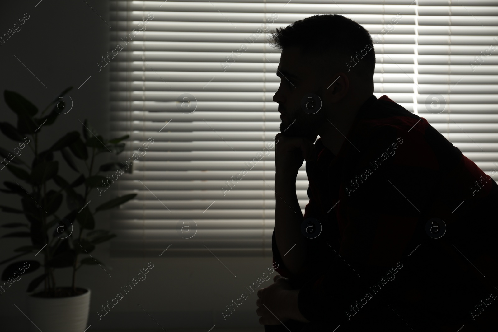 Photo of Silhouette of sad man near closed blinds indoors. Space for text