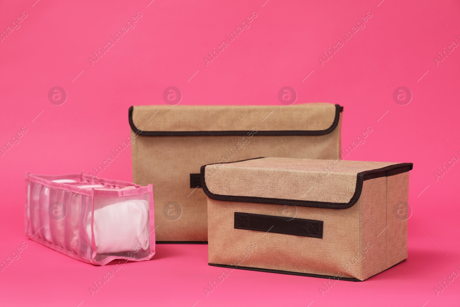 Photo of Textile storage cases and organizer with folded clothes on pink background