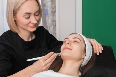 Photo of Cosmetologist applying mask on woman's face in clinic