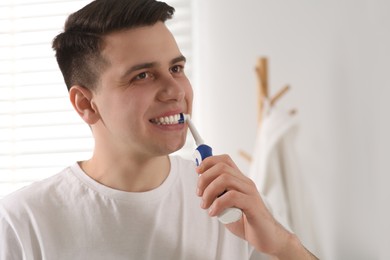 Photo of Man brushing his teeth with electric toothbrush in bathroom
